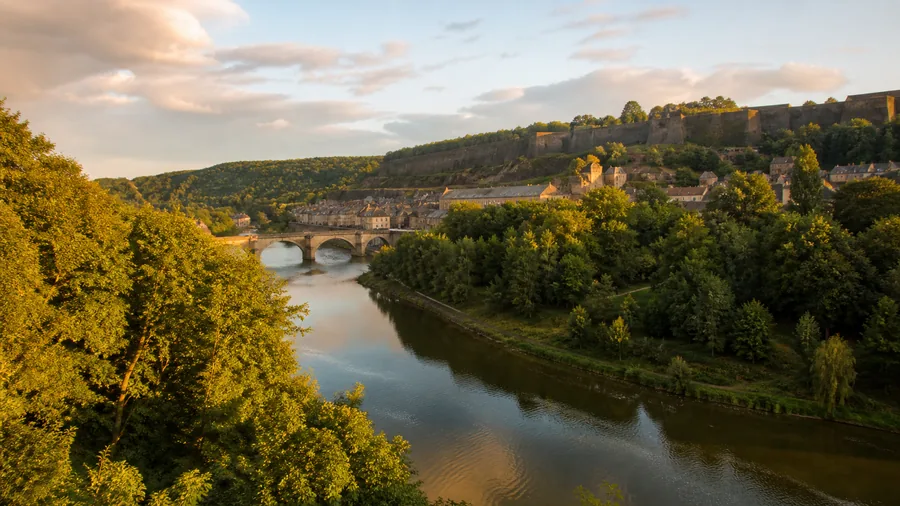 Ambiance romantique inspirée des Ardennes avec vallée de la Meuse, pont de pierre, forêt et forteresse au soleil bas